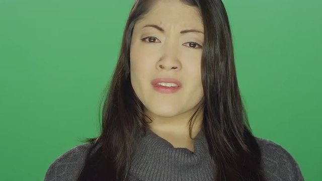 Beautiful young Asian woman sad and crying, on a green screen studio background