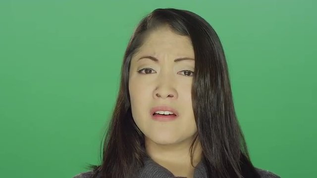 Beautiful young Asian woman sad and crying, on a green screen studio background