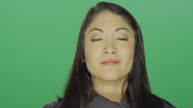 Beautiful young Asian woman looking hopeful, on a green screen studio background