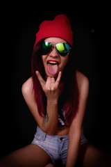 Attractive young woman in a pink knitted cap and sunglasses, showing tongue and making rock hand gesture