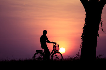 Man with bicycle in garden beautiful sunset and leafless tree