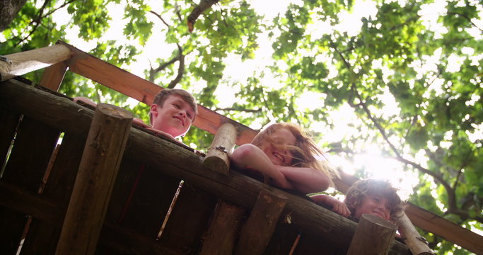 Children smiling over edge of treehouse with leaves above them