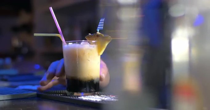 Closeup shot of glass with cocktail on bar counter, unseen barmen is putting drinking straws into it.
