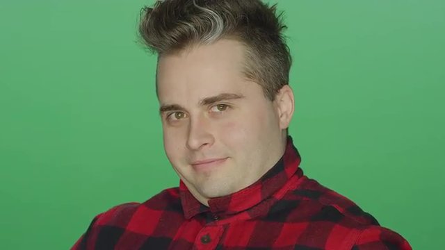 Young man winking and raising his eyebrows, on a green screen studio background