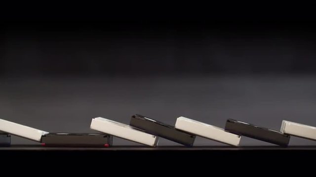 Slow motion clip of a row of mini DV tapes toppling like dominos.  Locked-off shot with black background, originally recorded in 4K at 60fps.