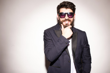 Cheerful young handsome man in sunglasses keeping hand on chin and looking at camera with smile...