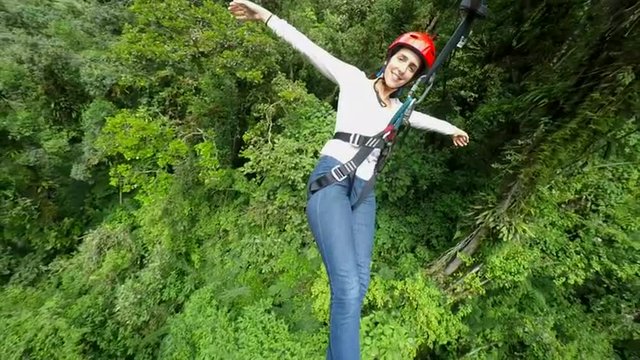 Experience the thrill of adventure as a young woman soars over the lush rainforest on a zipline,captured from a breathtaking third person perspective.