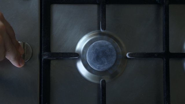 A man lights a gas stove top, he turns a switch and presses it
