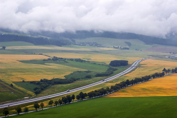 Beautiful autumn mountains landscape, road in  fields, cloudy sky