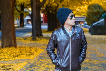 An Asian man in a brown jacket walks in a street
