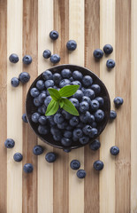Blueberries in black jar with green leves overhead on wooden cutting board in studio