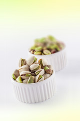 Pistachios roasted close up in two ceramic jars selective focus on white and green bright background in studio