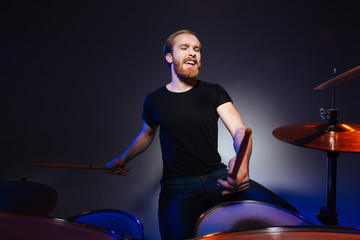 Attractive bearded man drummer playing drums with passion