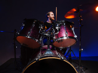Fototapeta na wymiar Attractive bearded man drummer sitting and playing on his kit