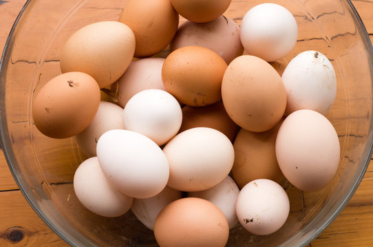 Top down view of natural looking brown and white freshly laid eggs in glass bowl on wooden table