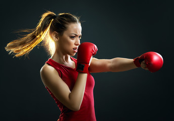 Fit, young, energetic woman boxing, black background