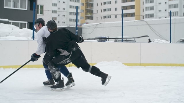 Two opposing hockey players in black and white uniforms competing for a puck during outdoor practice 