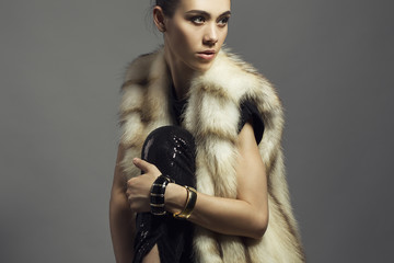 Sexy Beauty Girl with natural  Make up.  Fashion Brunette Portrait of a girl dressed in fur coat and black shirt posing on a grey background. Retro style
