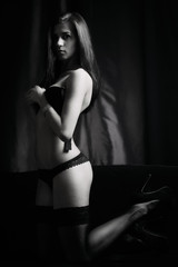 A girl in stockings and black lingerie kneeling on the chaise longue , removes her bra. Black and...