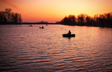 Beautiful landscape with orange sunrise, lake and fishermen 