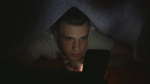 Attractive young man using a smart phone in bed