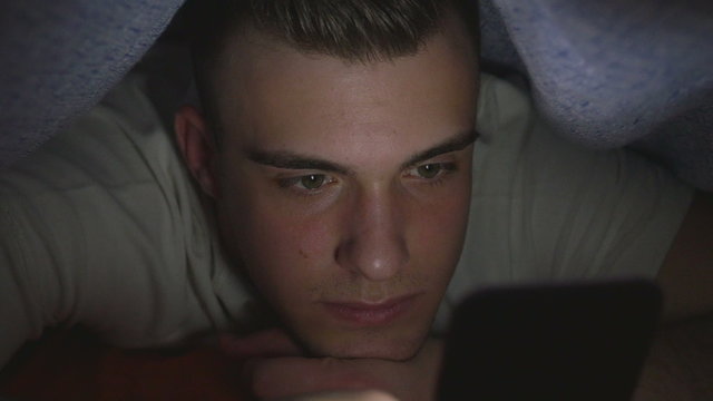 Attractive young man using a smart phone in bed