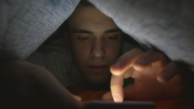 Attractive young man browsing social media on a smart phone in bed