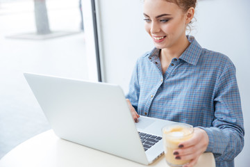 Cheerful woman drinking coffee and using laptop in cafe