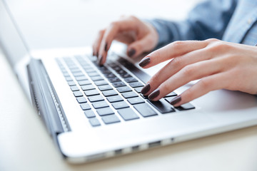 Hands of woman in blue shirt typing on laptop keyboard