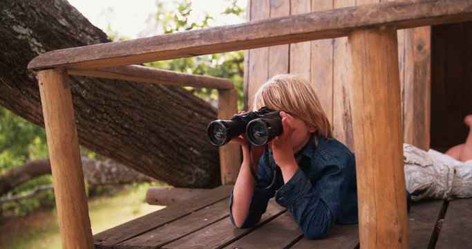 Boy lying in a treehouse looking through binoculars