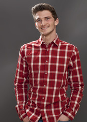 handsome smile - portrait of a friendly young male student with hands in pockets looking serious and happy, grey background studio