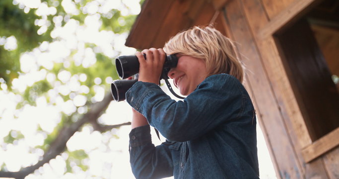 Boy sitting in a treehouse looking through binoculars
