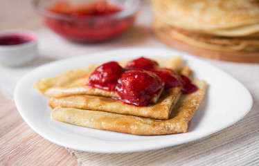 Thin Russian pancakes folded triangle with strawberry sauce on a white plate, close-up, side view
