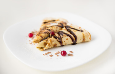 Thin pancakes folded triangle with berries and chocolate sauce on a white plate, white background, side view
