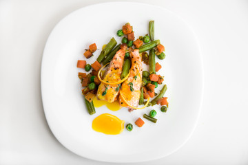 Baked salmon with green beans, carrots, green peas, thyme and orange sauce on a white plate, top view
