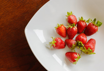 Ripe red strawberries in the plate on wooden table