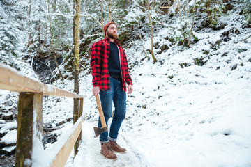 Handsome bearded lumberjack holding axe in mountain winter forest