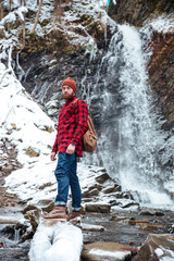 Fototapeta na wymiar Serious bearded young man standing near mountain waterfall in winter