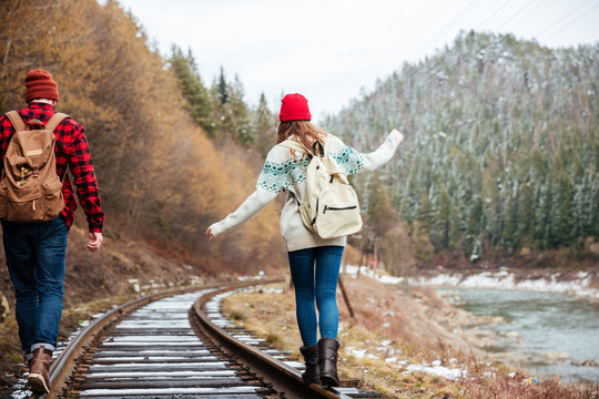 Beautiful young couple with backpacks walking along railroad