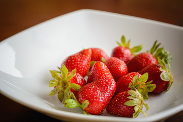 Ripe red strawberries in the plate on wooden table