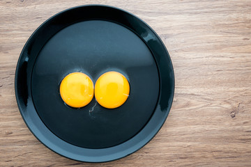 Top view of fresh eggs in black dish on wood background