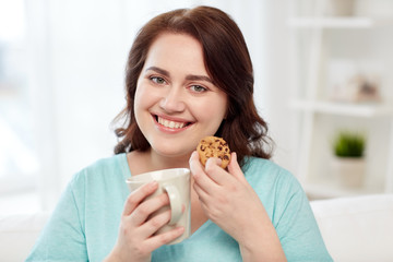 happy plus size woman with cup and cookie at home