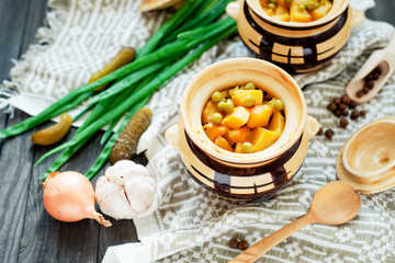 
National Russian , Ukrainian and Belarusian cuisine , baked potatoes with meat in the pot , onion , pepper, garlic , pickled cucumber and spices on a wooden background