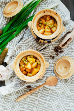 
National Russian , Ukrainian and Belarusian cuisine , baked potatoes with meat in the pot , onion , pepper, garlic , pickled cucumber and spices on a wooden background