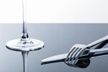 Messer, Gabel und ein Weinglas auf glänzender, spiegelnder Tischplatte