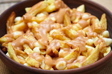 Poutine traditional homemade Canadian meal with fries, curd cheese, beer and gravy on vintage wooden table background. Close up view.