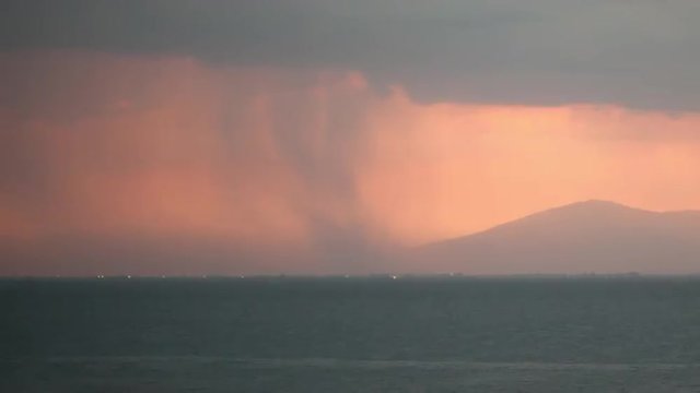 Timelapse shot of thunderstorm. Rain pouring from heavy clouds and lightnings striking over the coastal city and sea 
