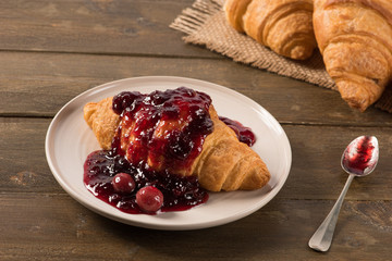 Breakfast croissant with cherry jam on a rustic background