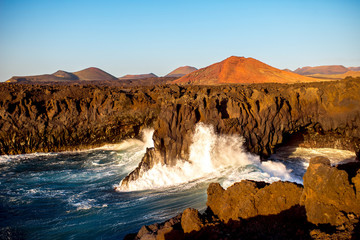 Los Hervideros rocky coast with wavy ocean and volcanos on the background on the sunset on Lanzarote island in Spain