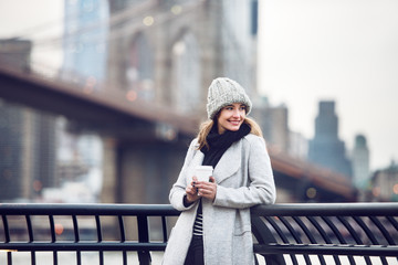 Happy smiling adult tourist woman holding paper coffee cup and enjoying the New York City view and Brooklyn bridge - 106508426